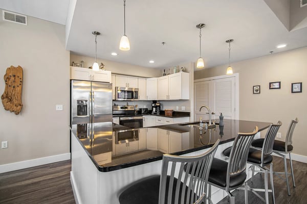 Modern kitchen with white cabinetry, stainless steel appliances, black granite countertops, and island seating with bar stools.